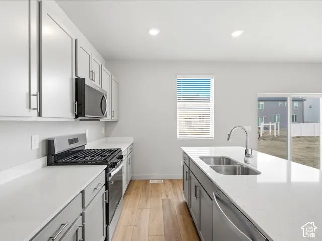Kitchen featuring light-toned cabinetry, quartz countertops, wood-finish flooring, stainless steel appliances, and a central island with a dual-basin sink