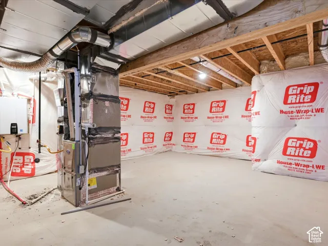 Unfinished basement featuring exposed wood joists, concrete floor, protective vapor barrier wall insulation, and a central forced-air furnace unit