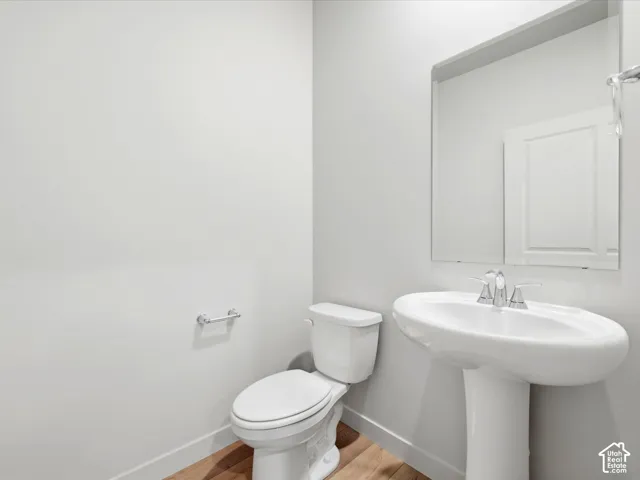 White pedestal sink with chrome faucet, large rectangular wall mirror, and wood-finish flooring