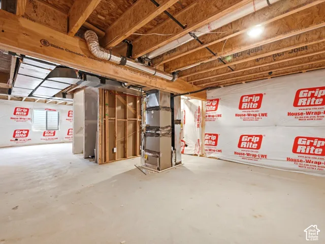 Unfinished basement featuring concrete flooring, exposed wooden joists, industrial HVAC system, and exterior house-wrap wall vapor barrier