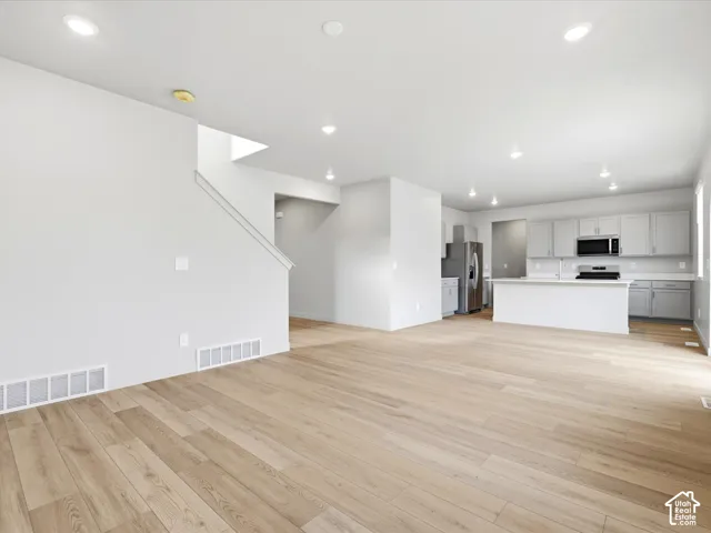 Open floor plan featuring wood-finish flooring, recessed lighting, cabinetry with neutral-finish doors, a kitchen island, and a built-in microwave