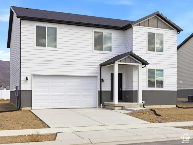 Two-story exterior featuring white horizontal siding, a gray concrete foundation base, gabled roofline with dark shingled eaves, a covered front entryway, and an attached two-car garage