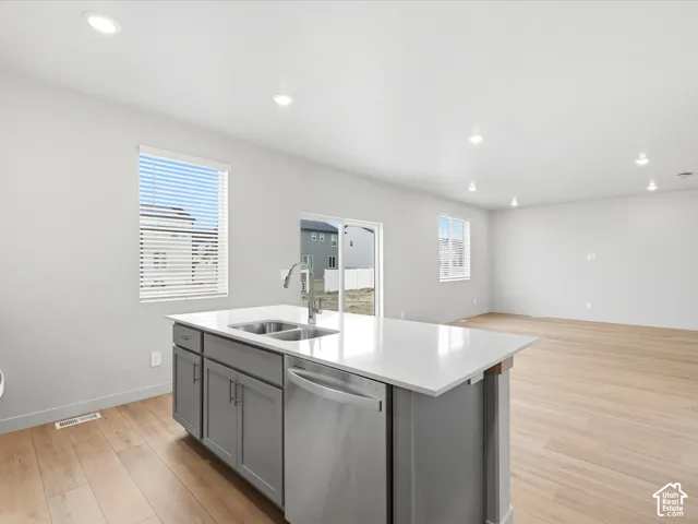 Kitchen island featuring a stone-composite countertop, dual-basin stainless steel sink, and shaker-style cabinetry, complemented by wood-finish flooring and recessed ceiling lighting