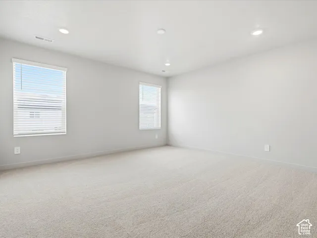 Neutral-toned interior space featuring wall-to-wall carpeting, recessed ceiling lighting, and dual windows with horizontal blinds