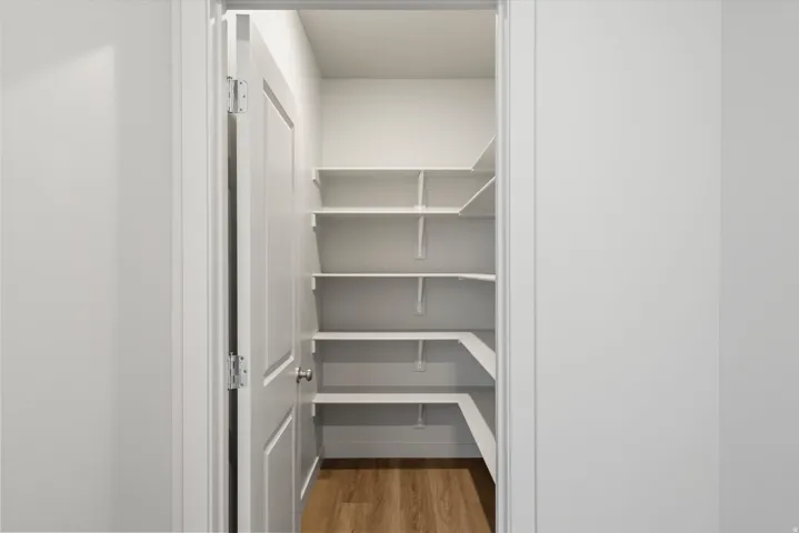 **DISCLAIMER** Interior package may vary. Spacious pantry with built-in shelving, wood-finish flooring, and a white paneled door