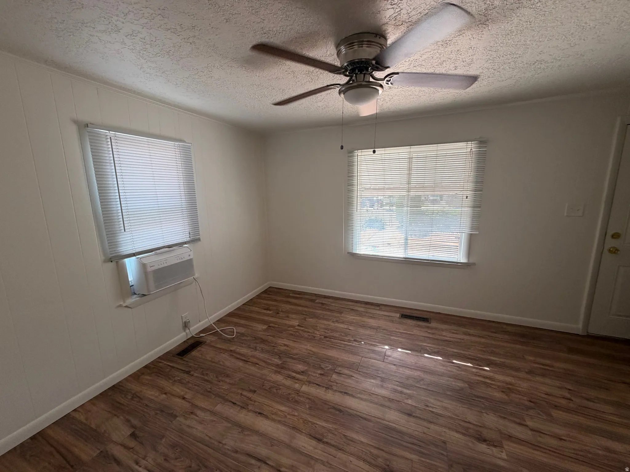 Wood-finish flooring with white baseboards, multiple windows with blinds, ceiling fan, and white walls