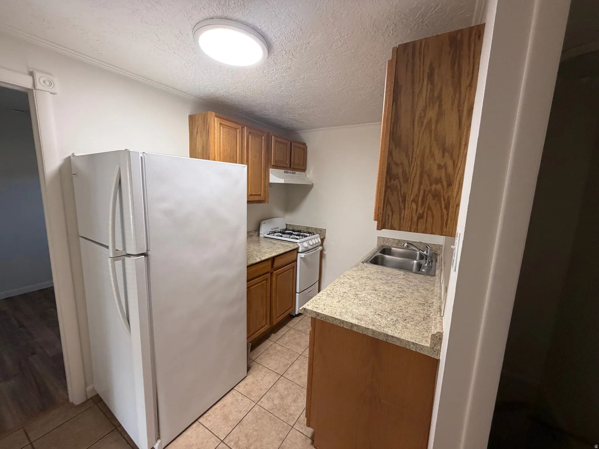 Compact kitchen featuring wood cabinetry, light-toned countertops, and a white appliance suite including a refrigerator and range