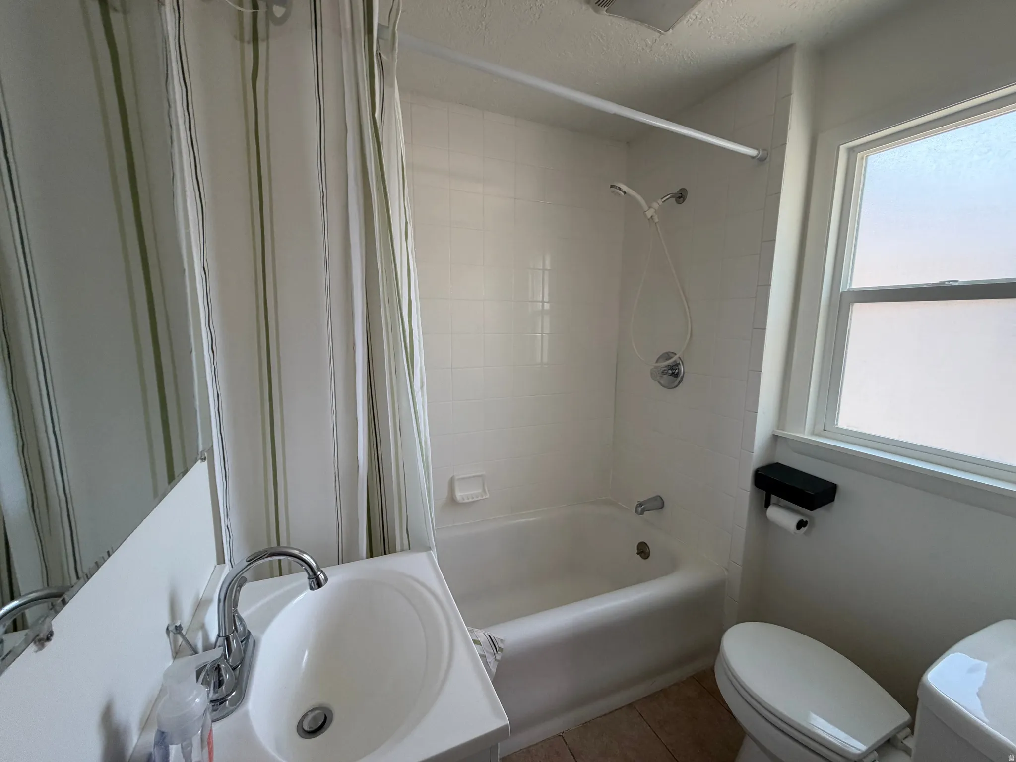 White tile shower surround, single-pane window, white vanity with integrated sink, chrome faucet, and wood-finish flooring