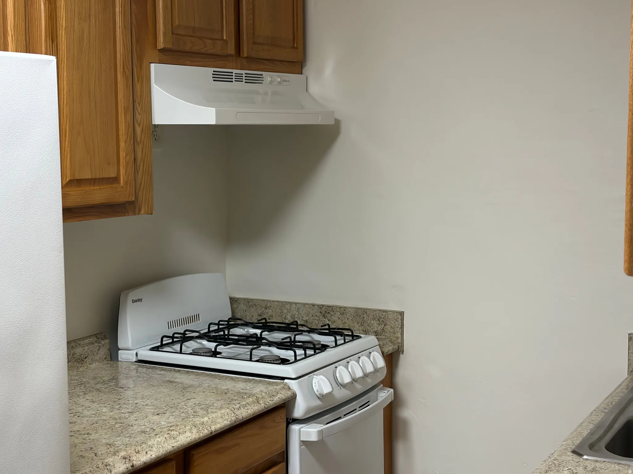 White freestanding gas range, light-toned countertops, wood-finish cabinetry, and a white range hood