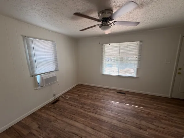 Wood-finish flooring with white baseboards, multiple windows with blinds, ceiling fan, and white walls