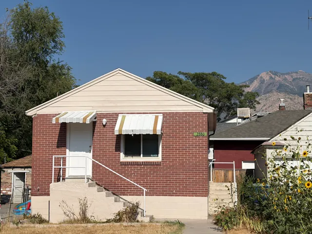 Brick exterior with white trim, featuring a gabled roofline and striped window awnings