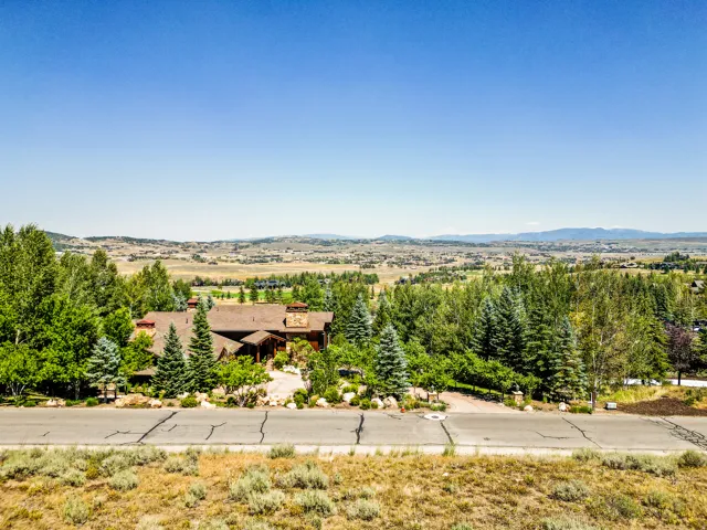 Expansive property featuring a brown multi-level exterior, an attached garage, a paved driveway, and mature landscaping