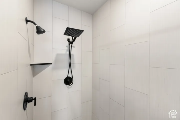 Shower with light-toned rectangular wall tiling, featuring a matte black rain shower head, additional shower head with hose, and built-in matte black shelf