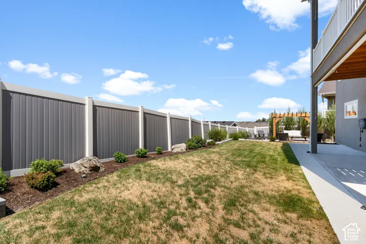 Fenced backyard featuring a concrete patio, a wooden pergola, and a landscaped garden bed with mature shrubs and decorative rocks