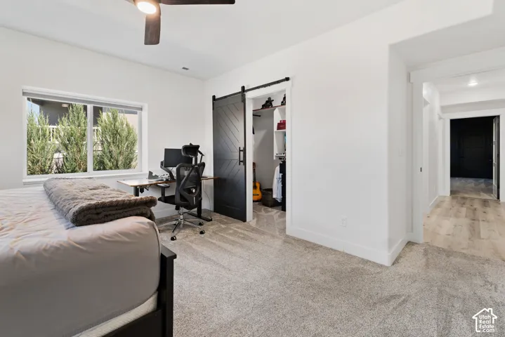 Carpeted interior space featuring a large window, a black barn door, a ceiling fan with integrated lighting, and a doorway leading to a hall with wood-finish flooring