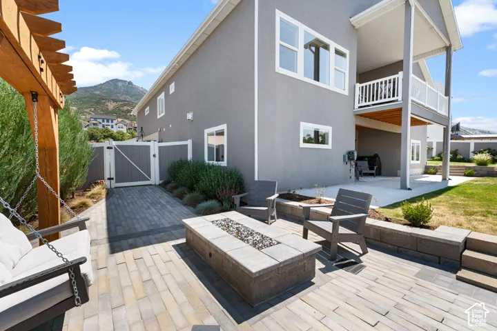 Expansive paved patio with a built-in fire pit, pergola, and an upper-level balcony