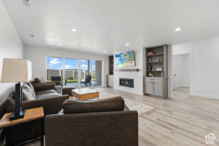 Spacious living area featuring light wood-finish flooring, recessed lighting, and a modern fireplace with a shiplap accent wall
