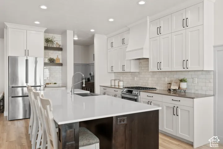 Gourmet kitchen featuring a substantial island with seating, stainless steel appliances, white shaker cabinetry, subway tile backsplash, and wood-finish flooring