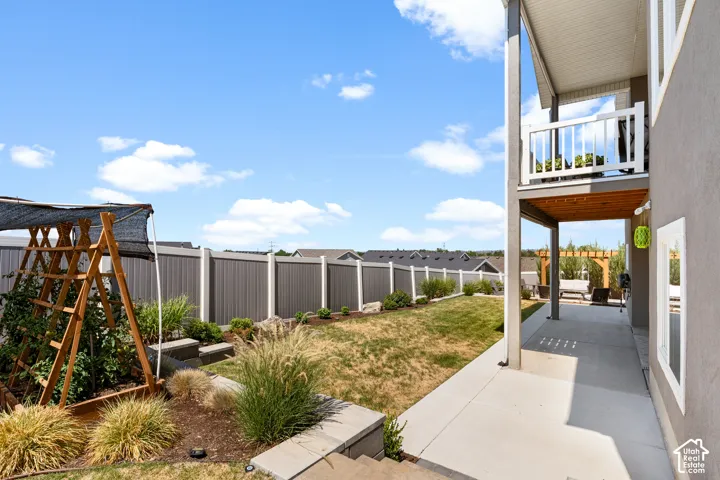 Expansive backyard featuring a concrete patio, second-story deck with white railing, and a privacy fence