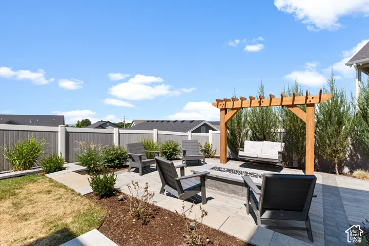Hardscaped patio area featuring a built-in fire pit, a natural wood pergola, and surrounding landscaping