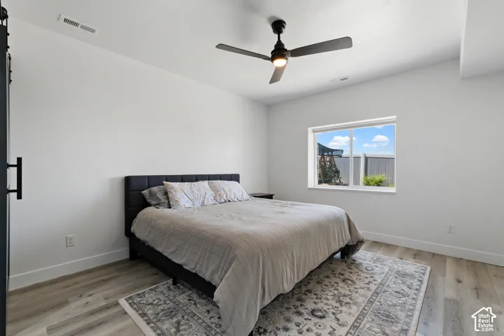 Bright room featuring light-toned wood-finish flooring, a contemporary ceiling fan, a window with a white frame, and a dark sliding barn door