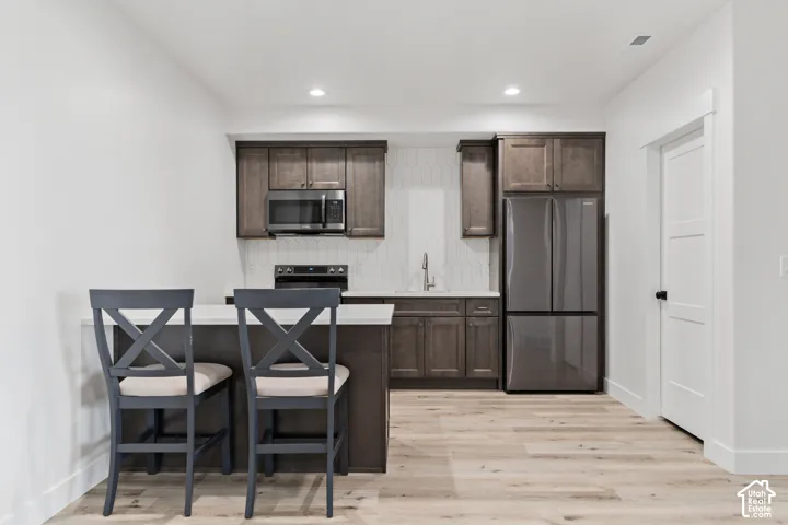Open-concept kitchen featuring wood-finish flooring, dark wood cabinetry, and a white backsplash