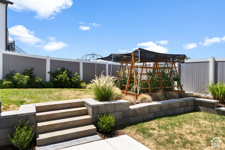 Tiered backyard featuring a garden bed with a wooden trellis, concrete block retaining walls, and stone steps