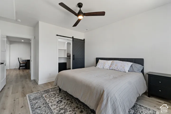 Spacious room featuring wood-finish flooring, a contemporary ceiling fan with integrated lighting, and a closet with a modern barn door