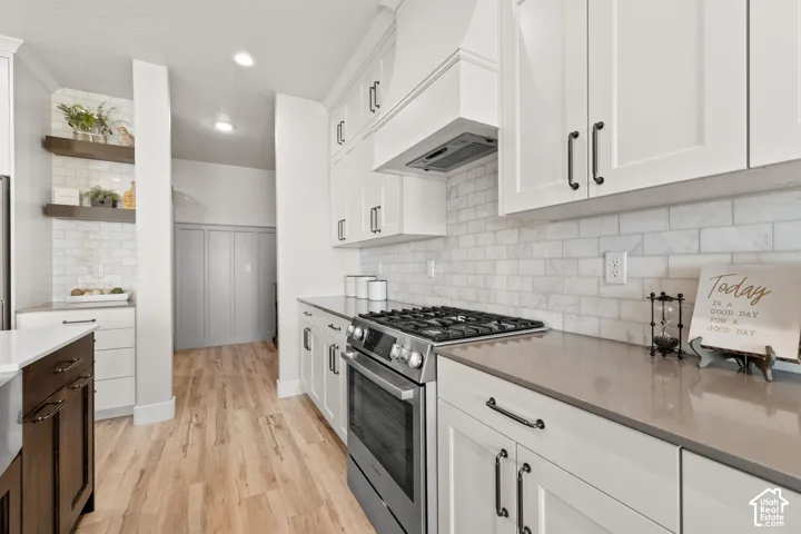 Modern kitchen featuring a stainless steel range, white shaker cabinetry, quartz countertops, white subway tile backsplash, and light wood-finish flooring