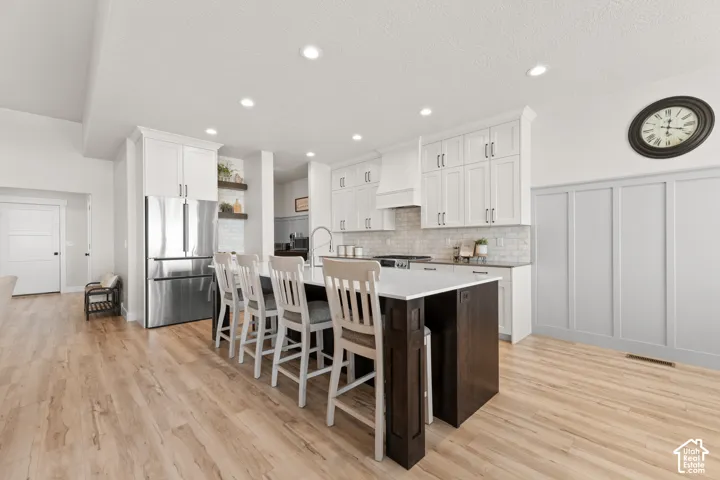 Modern kitchen featuring a large central island with seating, white shaker cabinetry, stainless steel appliances, recessed lighting, and wood-finish flooring