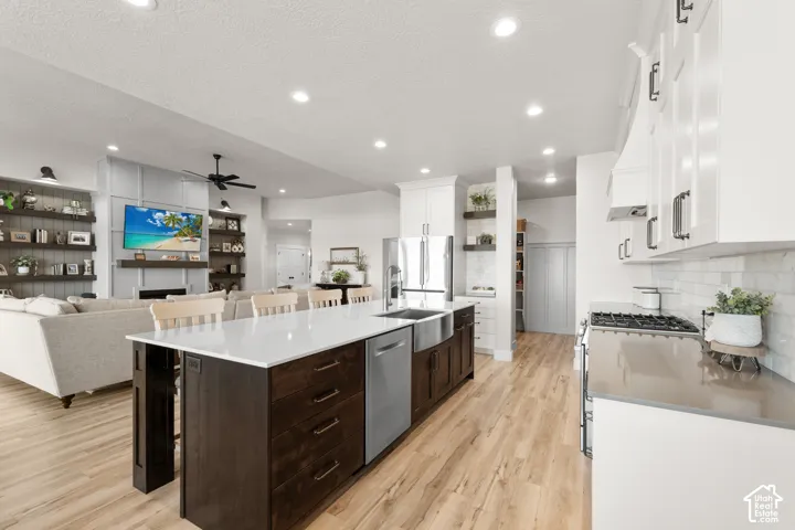 Open-concept kitchen featuring a dark wood island with white countertop, stainless steel appliances, white cabinetry, and wood-finish flooring
