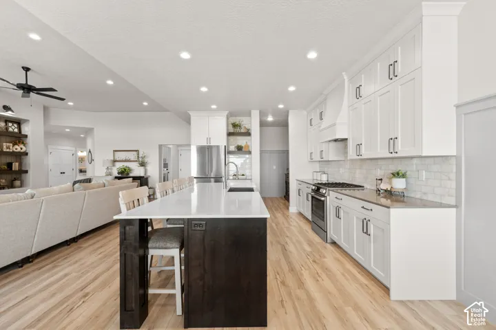 Spacious kitchen featuring an oversized island with counter seating, wood-finish flooring, white shaker cabinetry, stainless steel appliances, and a subway tile backsplash