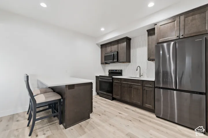 Contemporary kitchen featuring dark wood cabinetry, stainless steel appliances, light wood-finish flooring, a white countertop, and a white hexagonal tile backsplash