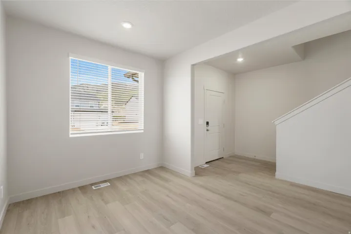 Bright, open room featuring expansive windows with horizontal blinds flooding the space with natural light, wood-finish flooring throughout, and clean white walls with recessed ceiling lighting
