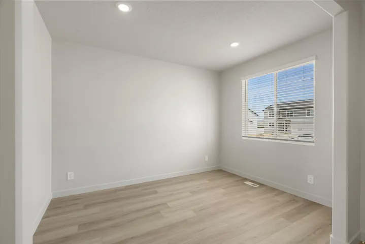 Bright, light-filled bedroom with wood-finish flooring, recessed ceiling lighting, and large windows with plantation shutters offering natural illumination and privacy