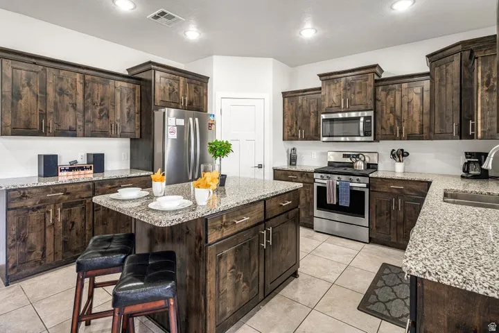 Kitchen featuring dark wood cabinetry, light-toned countertops, stainless steel appliances, a center island, and tile flooring