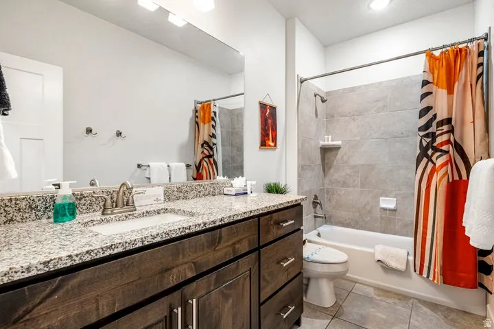 Granite countertop with undermount sink, dark wood-finish vanity, large mirror, tile-surround bathtub, and tiled flooring