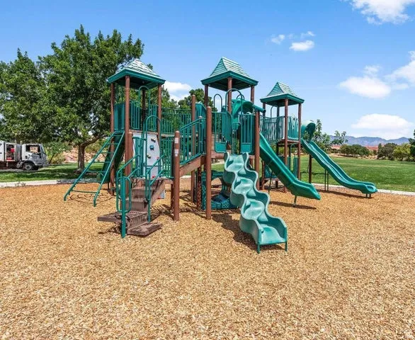 Multi-level playground structure featuring three turrets with green metal roofing, multiple slides in varying heights, climbing elements, and tube features, all set on a protective engineered wood fiber surface