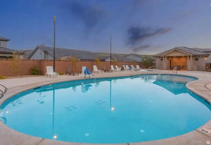 Curved swimming pool with concrete decking, surrounding a covered cabana structure featuring stone accents and recessed lighting