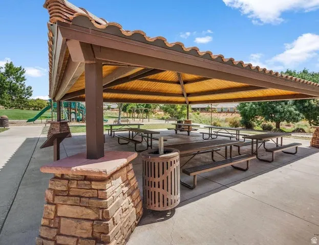 Expansive covered pavilion with wood-beam construction and yellow fabric shade canopy, featuring multiple picnic tables with attached benches and brick-base support column