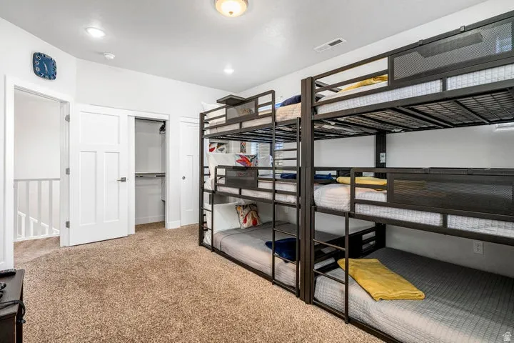 Spacious bedroom featuring built-in bunk bed structures with metal frames and integrated shelving, carpeted flooring, recessed ceiling lighting, and direct access to a walk-in closet with shelving systems