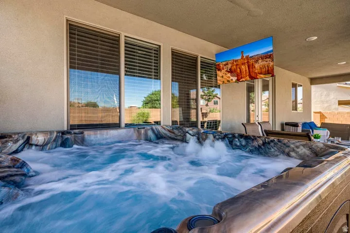 Outdoor spa with integrated water feature, covered patio, mounted television, and sliding glass doors