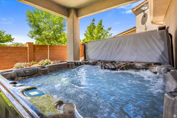 Patio featuring a hot tub with an open cover, brick privacy wall, and mature landscaping