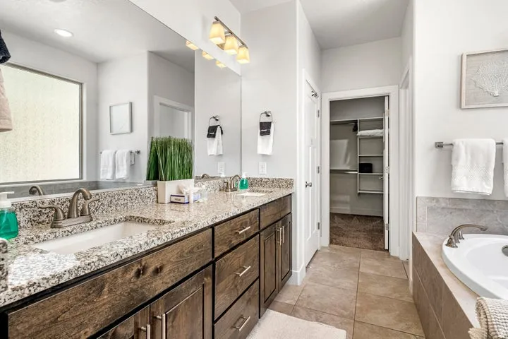 Dual vanity with granite countertops, rich wood-finish cabinetry, and an integrated soaking tub