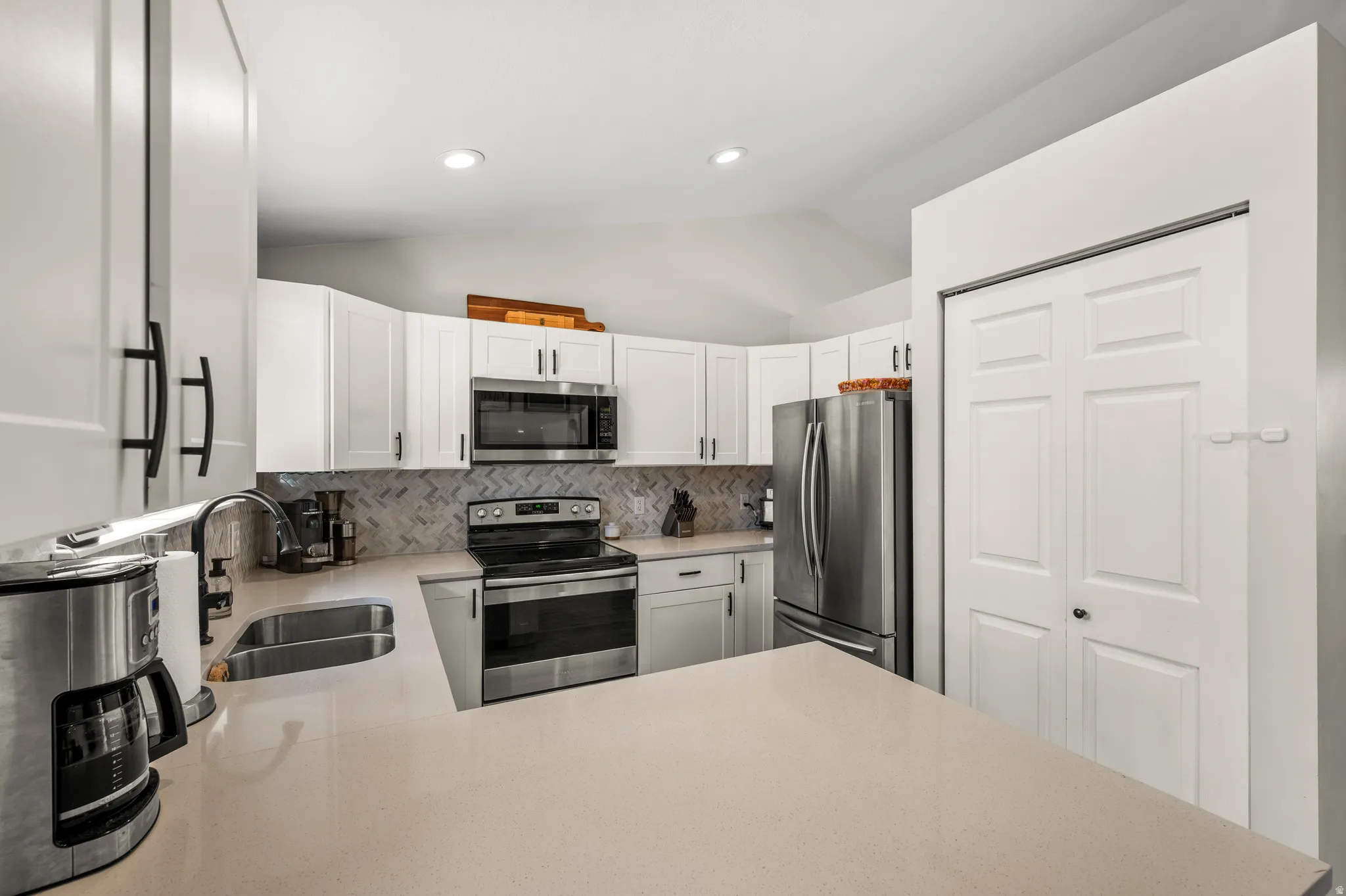 Modern kitchen featuring white cabinetry, stainless steel appliances, a herringbone tile backsplash, light-toned countertops, and recessed lighting