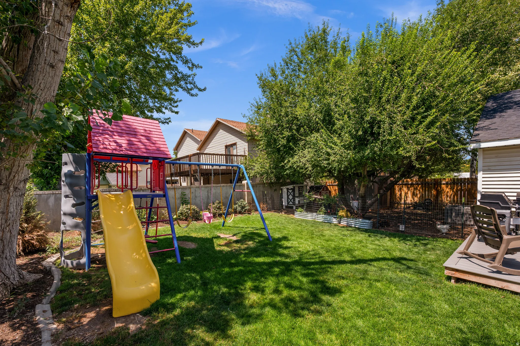 Expansive backyard featuring a manicured lawn, a wooden deck, and mature trees