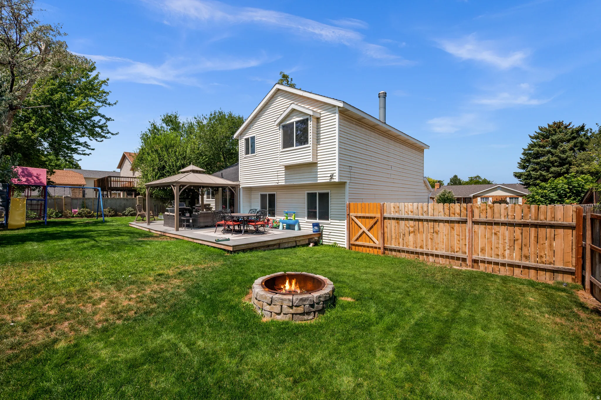 Expansive backyard featuring a stone-ringed fire pit, a spacious wood deck, and a privacy fence