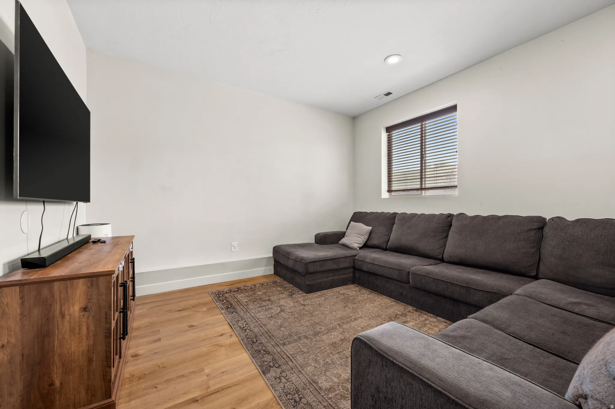 Spacious entertainment room featuring a sectional seating area, wood-finish flooring, area rug, and wall-mounted flat-screen television