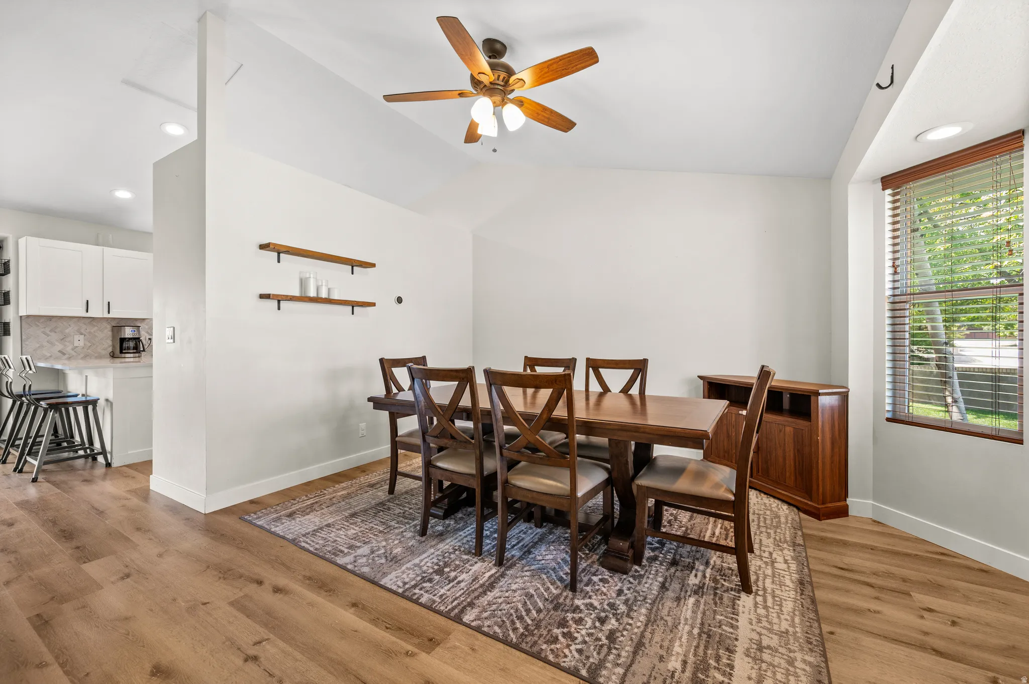 Dining area featuring wood-finish flooring, vaulted ceiling with a fan light fixture, and a large window with horizontal blinds
