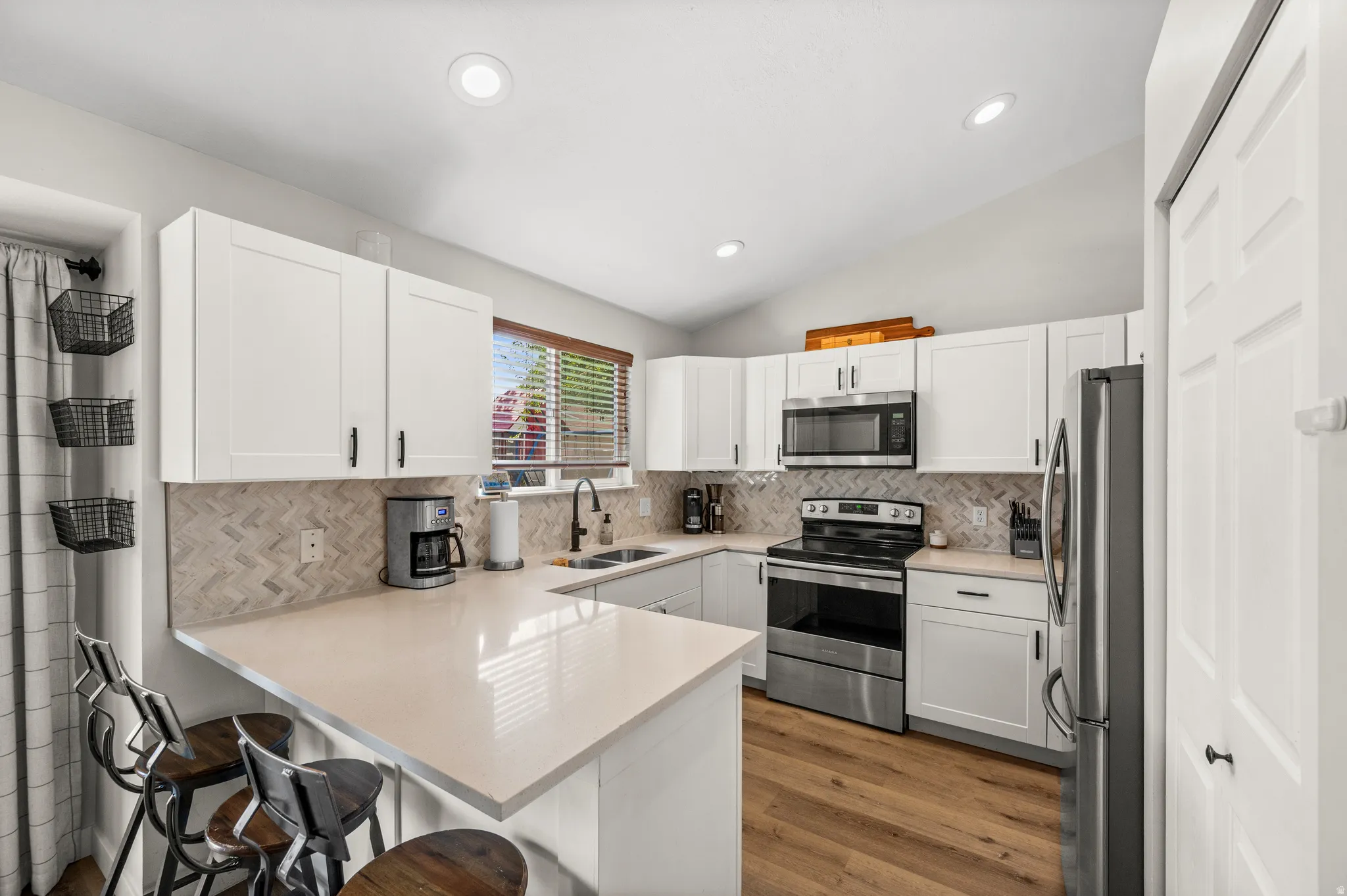 Kitchen featuring light countertops, white cabinetry with dark hardware, stainless steel appliances, a herringbone tile backsplash, and wood-finish flooring